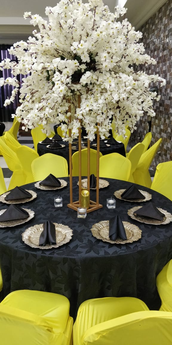 A dinner table set with black linen, gold chargers and a blossom centerpiece