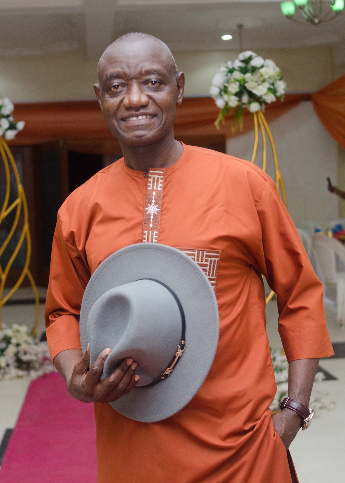 A gentleman in terracotta native attire holding a grey hat