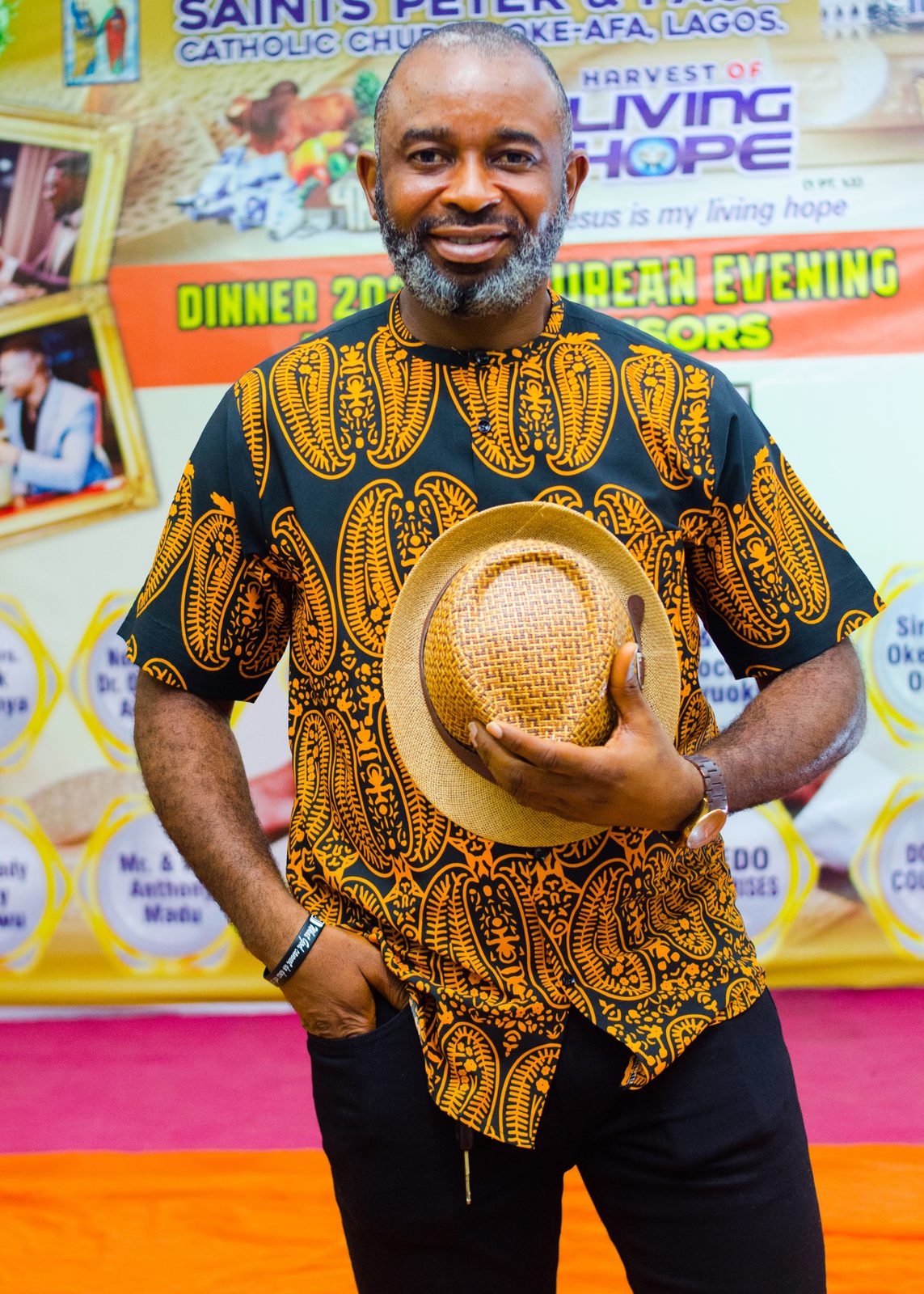 A guest in a patterned outfit holding a straw hat, all smiles